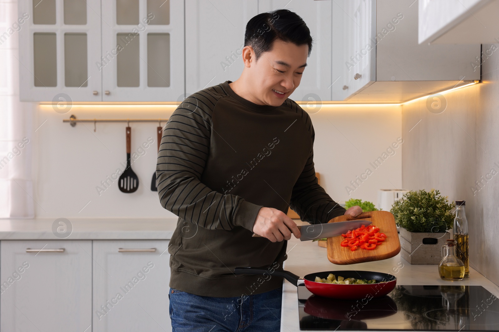 Photo of Cooking process. Man adding cut bell pepper into frying pan in kitchen, space for text