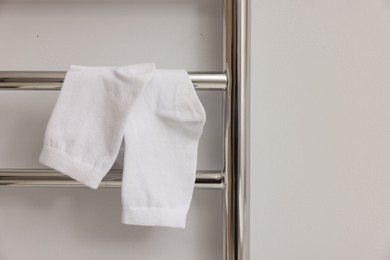 Photo of Heated towel rail with socks on white wall, closeup. Space for text