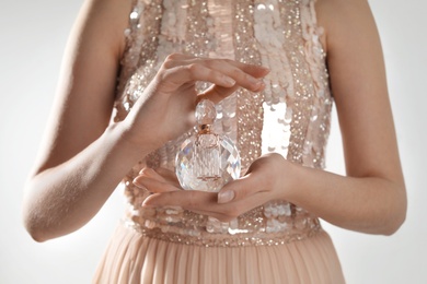 Young woman with bottle of perfume on light background, closeup