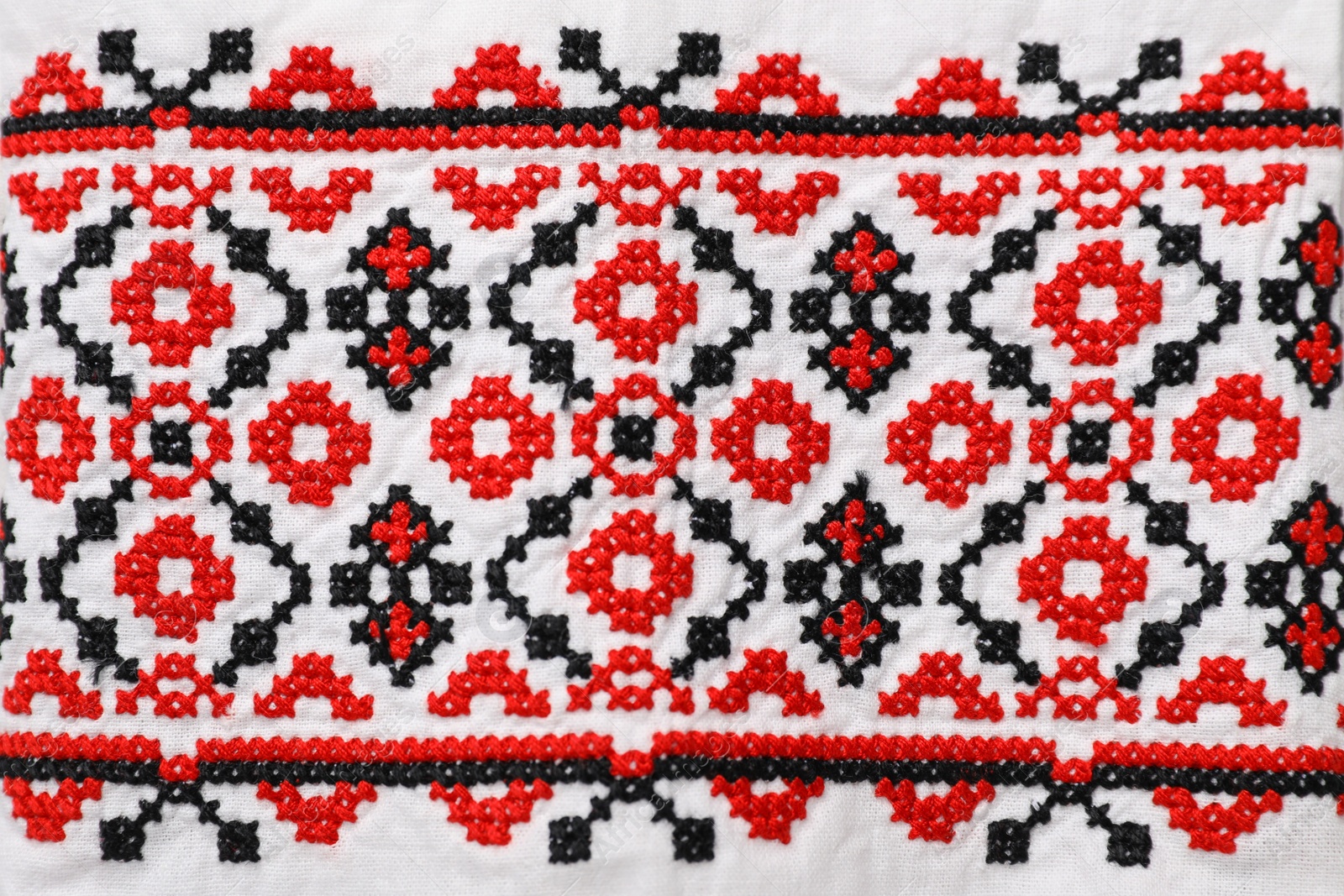 Photo of Beautiful red Ukrainian national embroidery on white fabric, top view