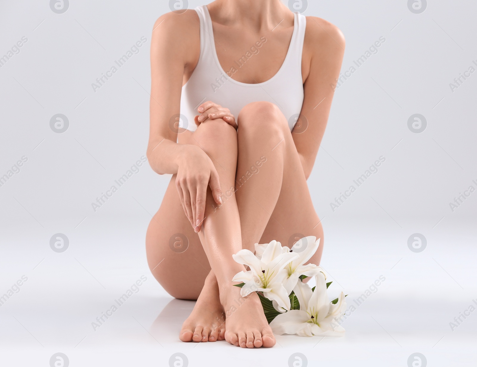 Photo of Young woman with beautiful silky body and flowers on light background