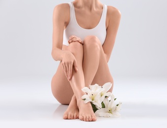 Young woman with beautiful silky body and flowers on light background