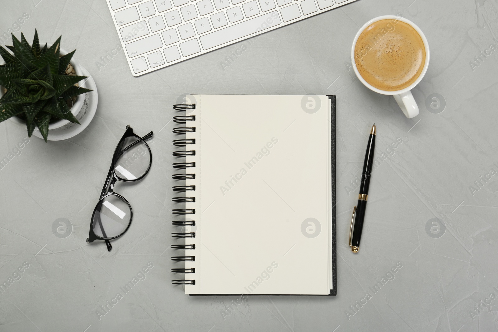 Photo of Open notebook, stationery, coffee and glasses on light grey table, flat lay