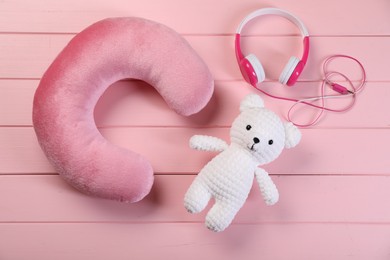 Photo of Travel pillow, toy bear and headphones on pink wooden background, flat lay