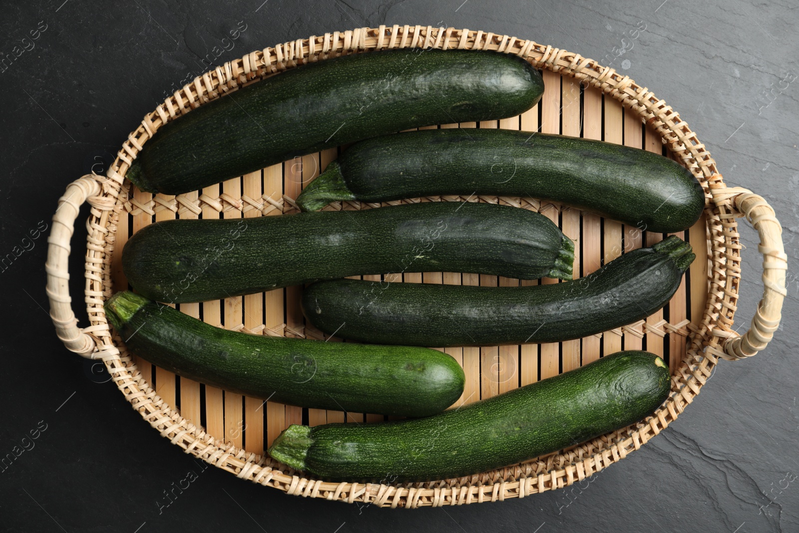 Photo of Basket with green zucchinis on black slate table, top view