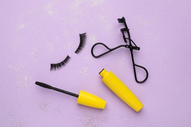 Photo of False eyelashes, curler and mascara on violet background, flat lay
