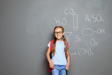 Photo of Little school child with backpack and chemical formulas on grey background