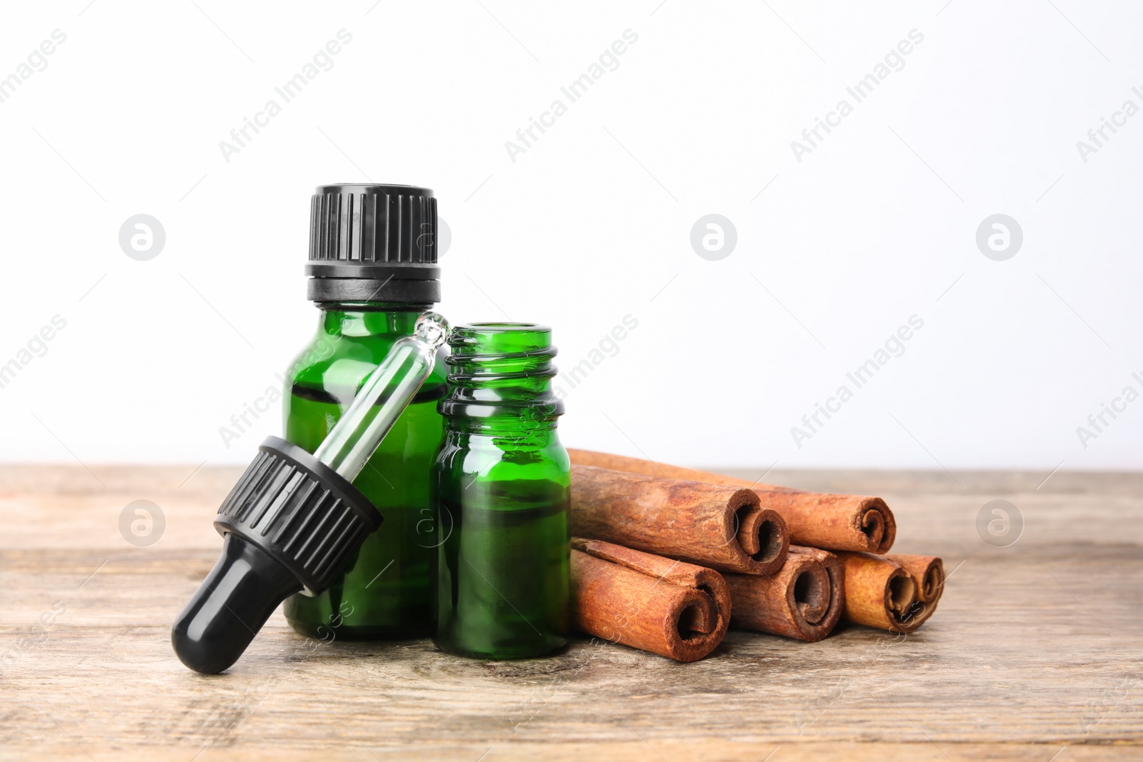 Photo of Bottles of essential oils and cinnamon sticks on wooden table against white background