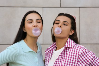 Photo of Beautiful women blowing gums near wall outdoors