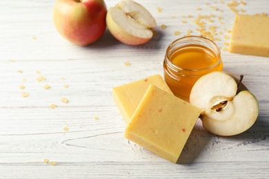 Handmade soap bars, apple and jar of honey on table. Space for text