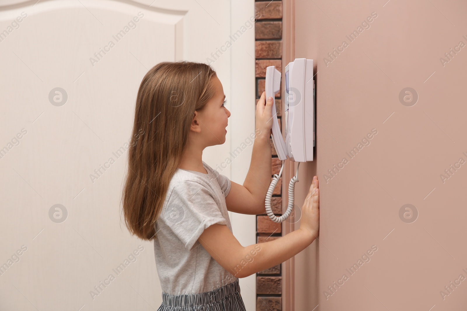 Photo of Cute little girl answering intercom call indoors