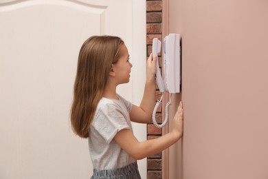 Photo of Cute little girl answering intercom call indoors