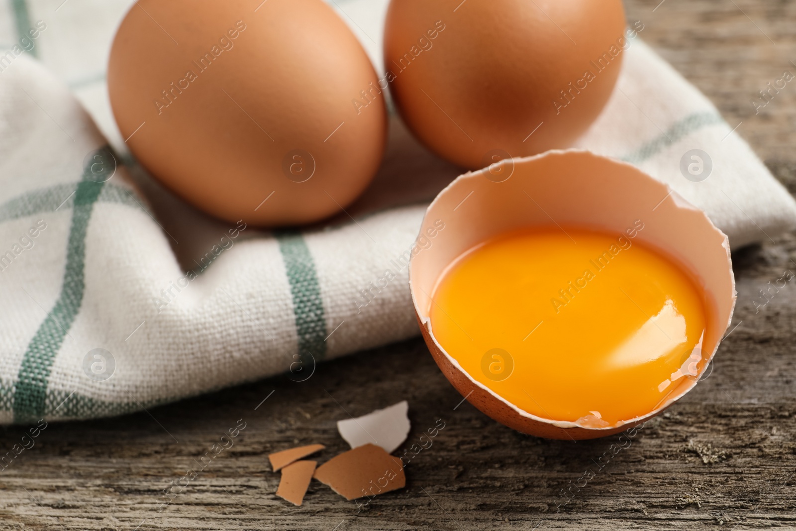 Photo of Raw chicken eggs and shell with yolk on wooden table, closeup