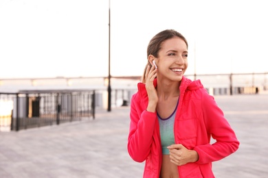 Photo of Young woman with wireless headphones listening to music outdoors. Space for text