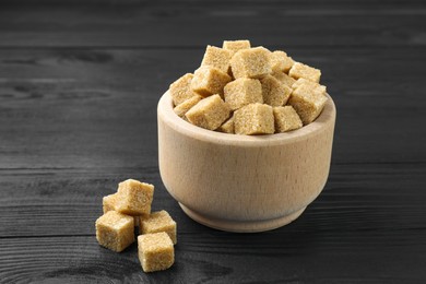 Photo of Brown sugar cubes in bowl on black wooden table