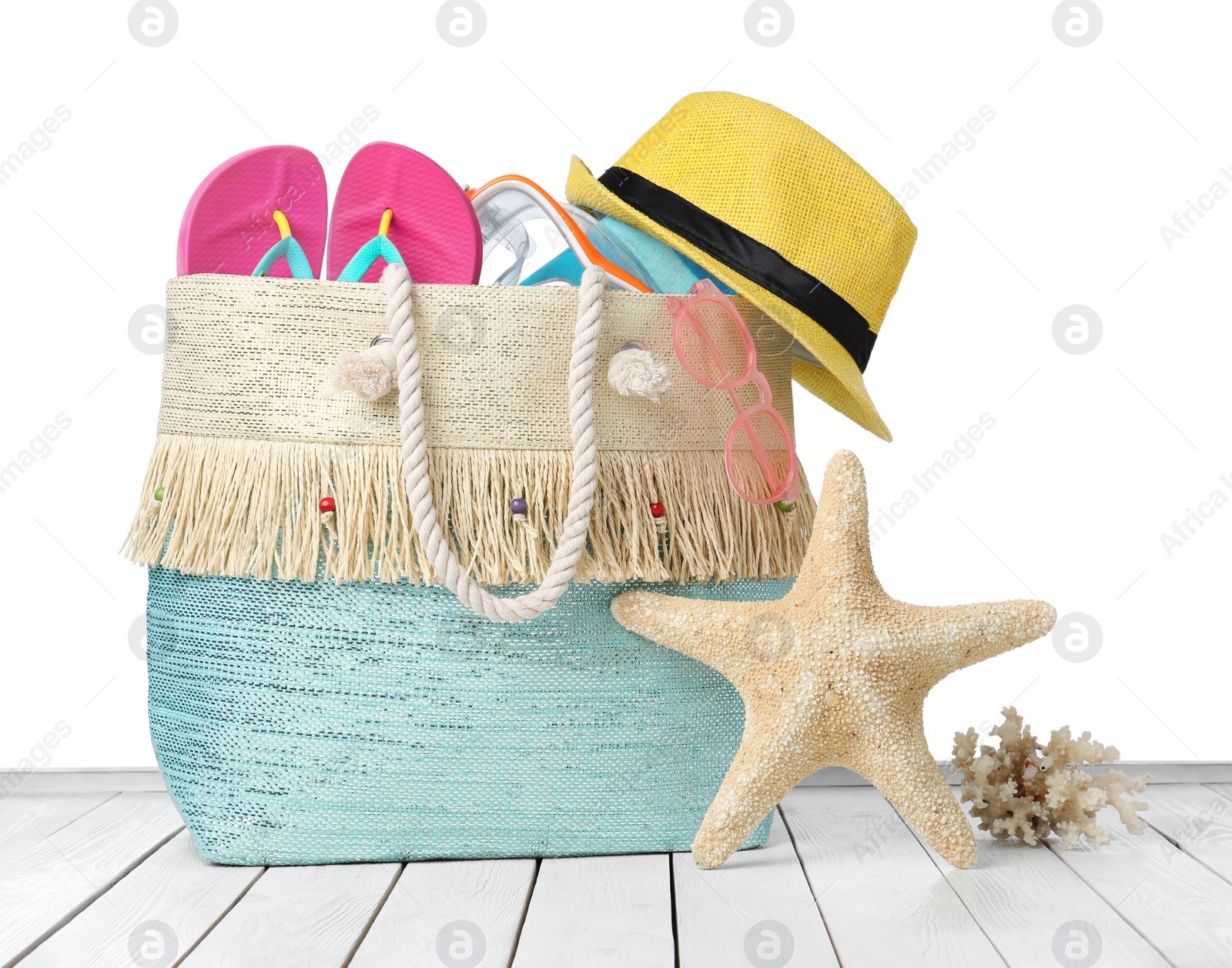 Photo of Stylish bag with beach accessories on wooden table against white background