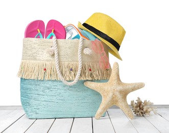 Photo of Stylish bag with beach accessories on wooden table against white background