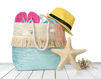 Stylish bag with beach accessories on wooden table against white background