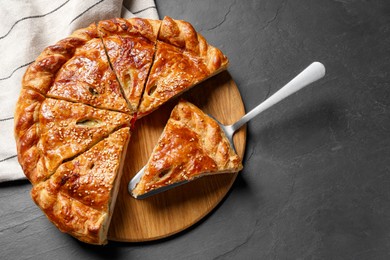 Cut delicious homemade pie and server on black table, top view