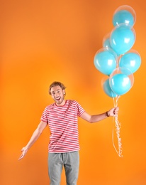 Young man with air balloons on color background
