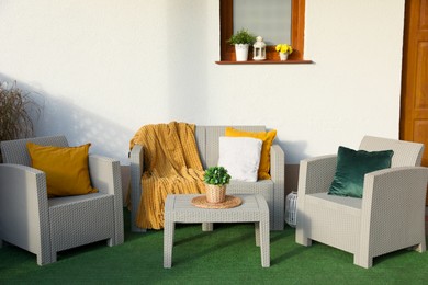 Beautiful rattan garden furniture, soft pillows, blanket and houseplant near white wall