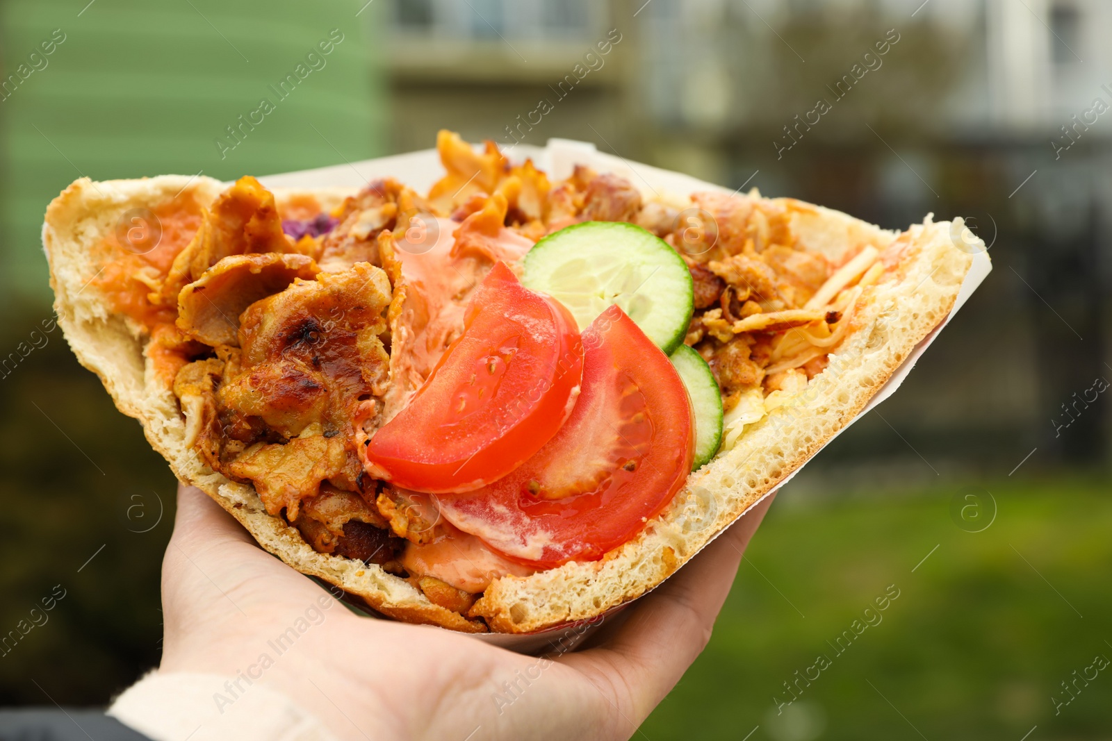 Photo of Woman holding delicious bread with roasted meat and vegetables outdoors, closeup. Street food