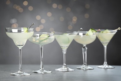 Glasses of martini with cucumber on grey table against blurred lights