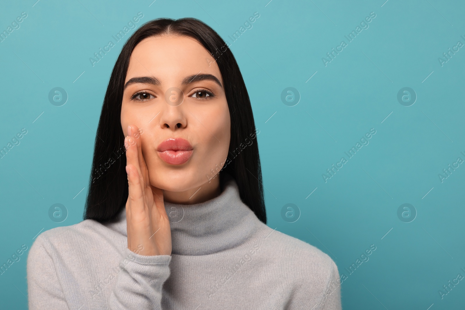 Photo of Beautiful young woman blowing kiss on light blue background. Space for text