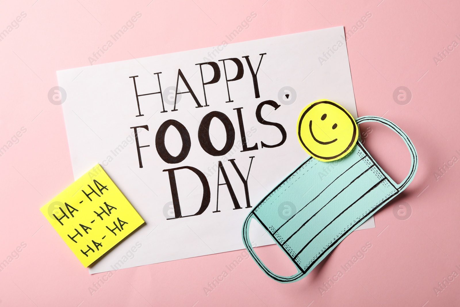 Photo of Paper mask and Happy Fools' Day note on pink background, flat lay