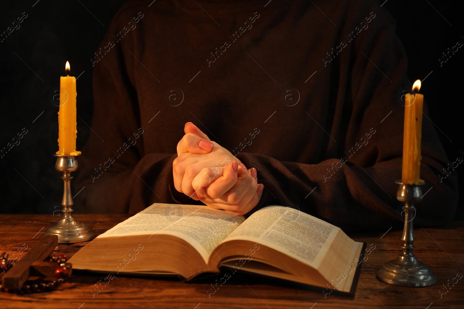 Photo of Woman praying at table with burning candles and Bible, closeup