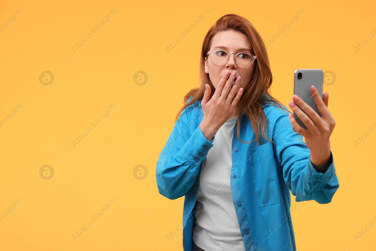 Photo of Emotional woman in eyeglasses taking selfie on orange background. Space for text