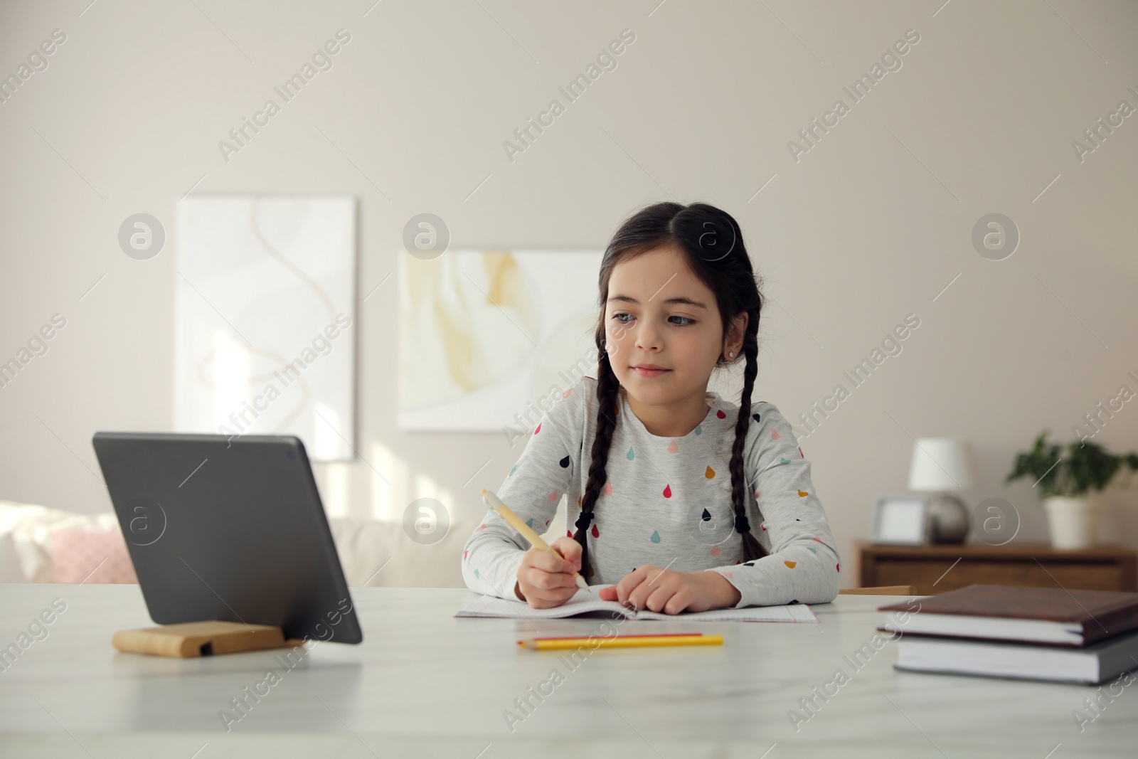 Photo of Little girl doing homework with modern tablet at home