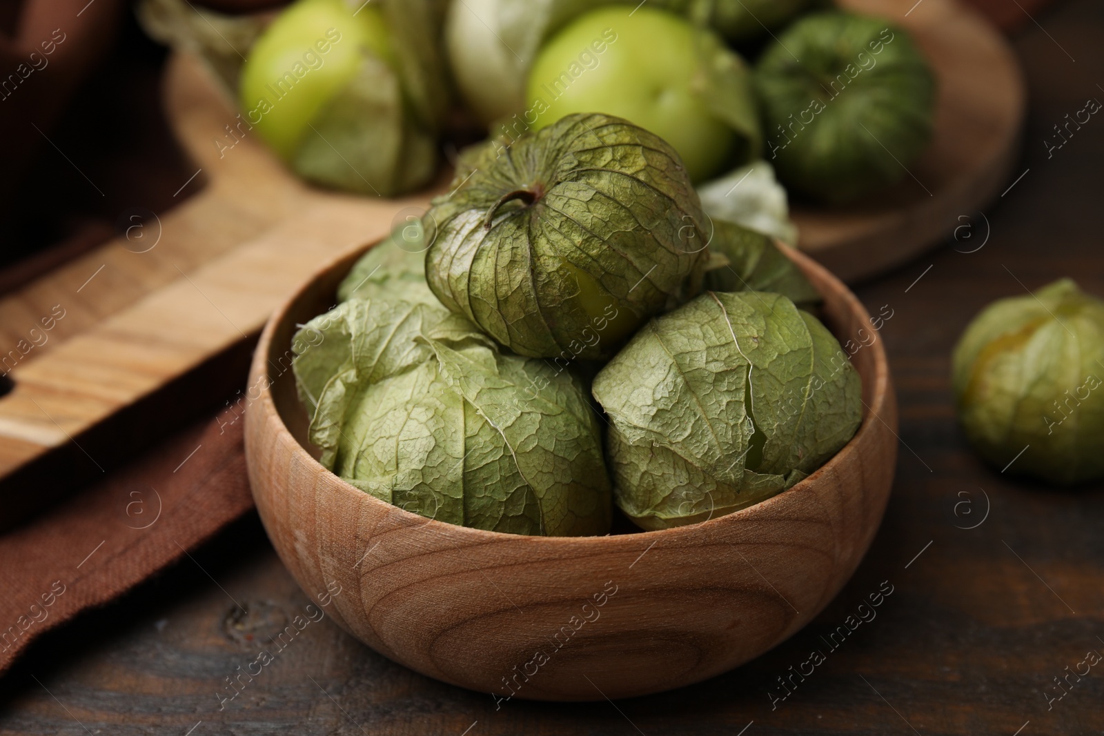 Photo of Fresh green tomatillos with husk in bowl on wooden table, closeup