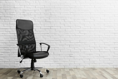 Comfortable office chair near white brick wall indoors. Space for text