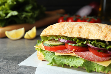 Photo of Delicious sandwich with fresh vegetables and salami on grey table, closeup