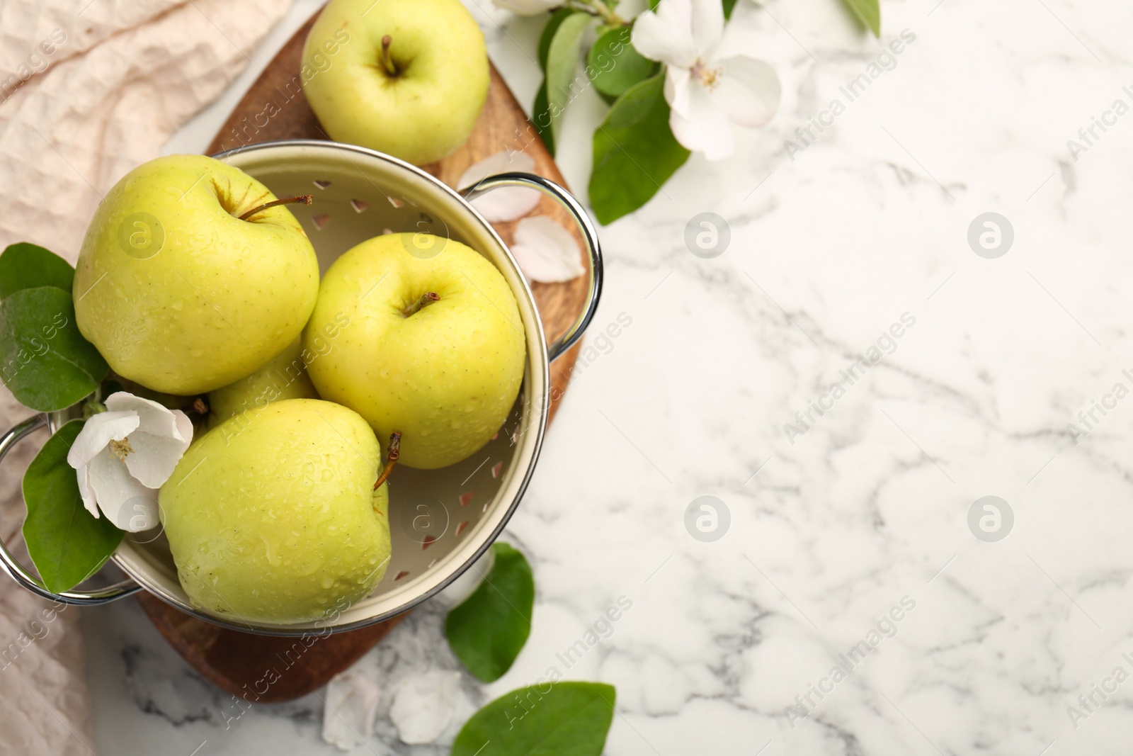 Photo of Colander with fresh apples and beautiful spring blossoms on white marble table, flat lay. Space for text