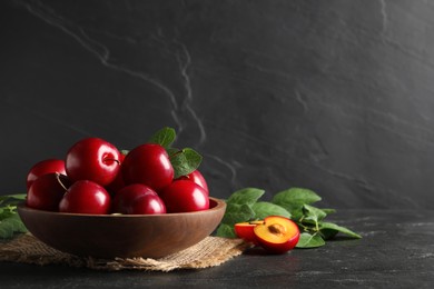 Photo of Delicious ripe cherry plums with leaves on black table. Space for text