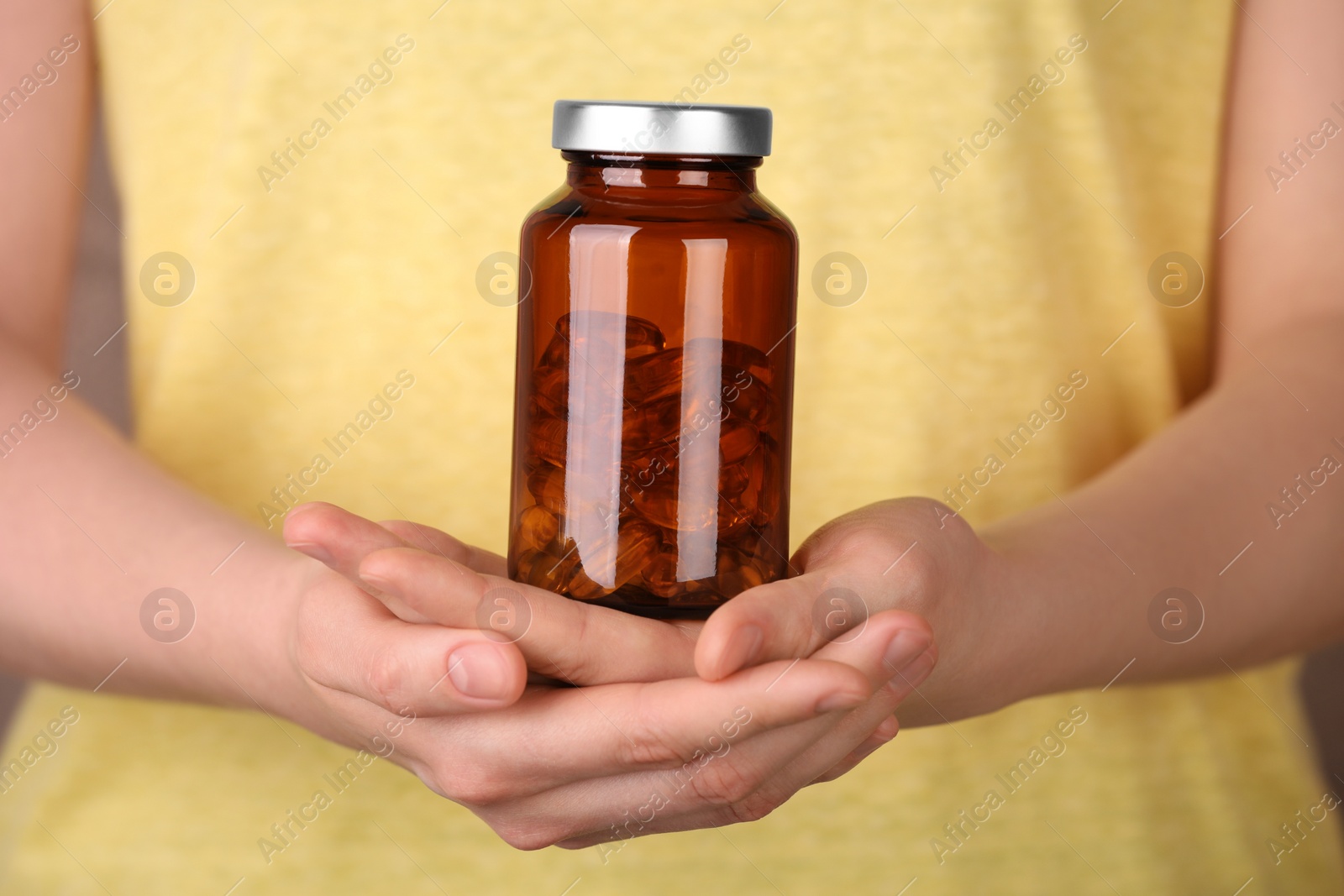 Photo of Woman holding bottle with vitamin capsules against light brown background, closeup