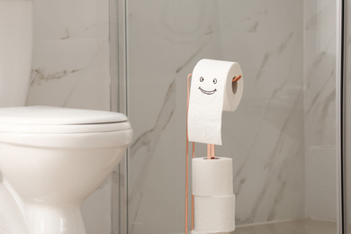 Photo of Modern toilet bowl and paper with funny face in bathroom