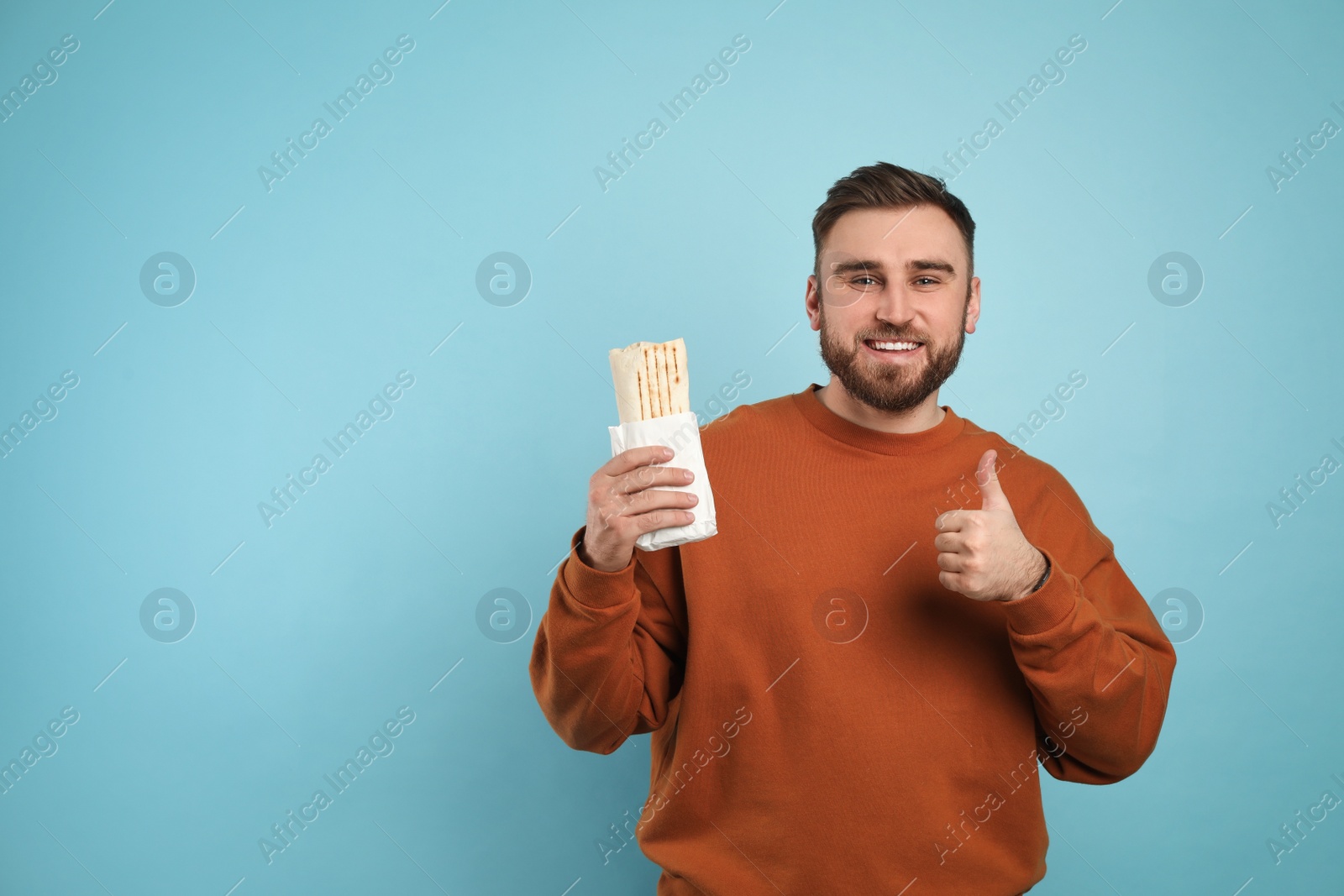 Photo of Young man with delicious shawarma on turquoise background, space for text