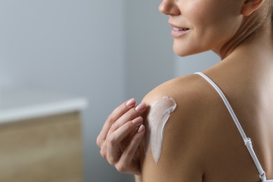 Photo of Woman applying body cream onto shoulder indoors, closeup. Space for text