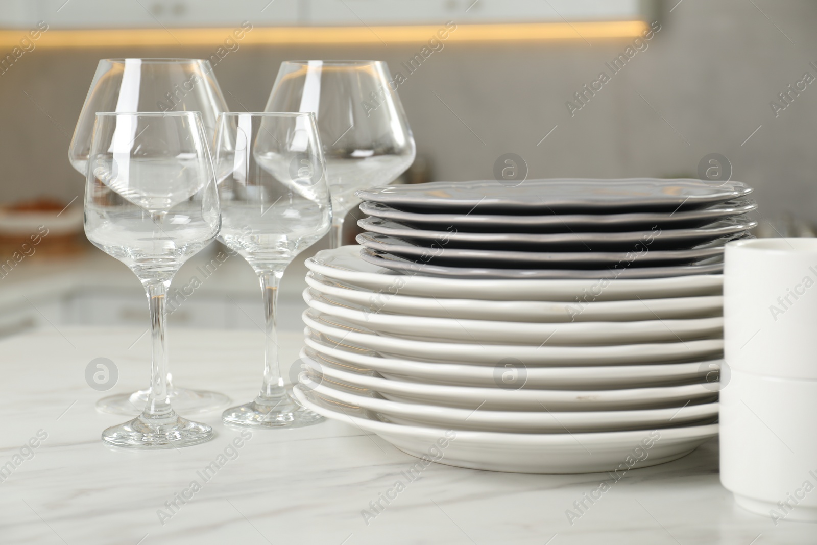 Photo of Clean plates and glasses on white marble table in kitchen