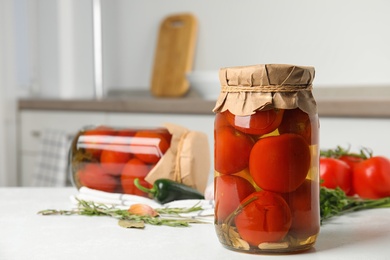 Photo of Pickled tomatoes in glass jars and products on white table