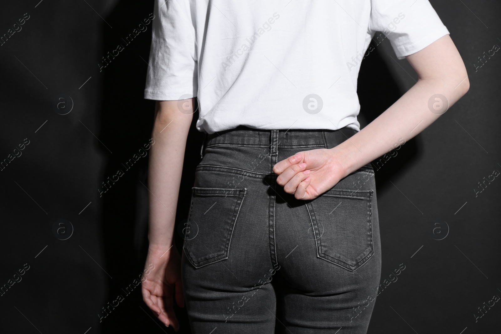 Photo of SOS gesture. Woman showing signal for help behind her back on black background, back view