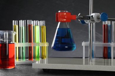 Retort stand and laboratory glassware with liquids on table against grey background, closeup