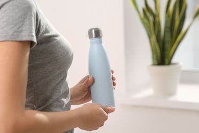 Woman holding thermo bottle indoors, closeup. Space for text