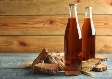 Photo of Bottles of delicious fresh kvass, spikelets and bread on blue wooden table. Space for text