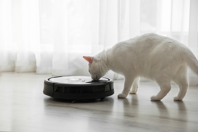 Photo of Modern robotic vacuum cleaner and cute cat on floor indoors