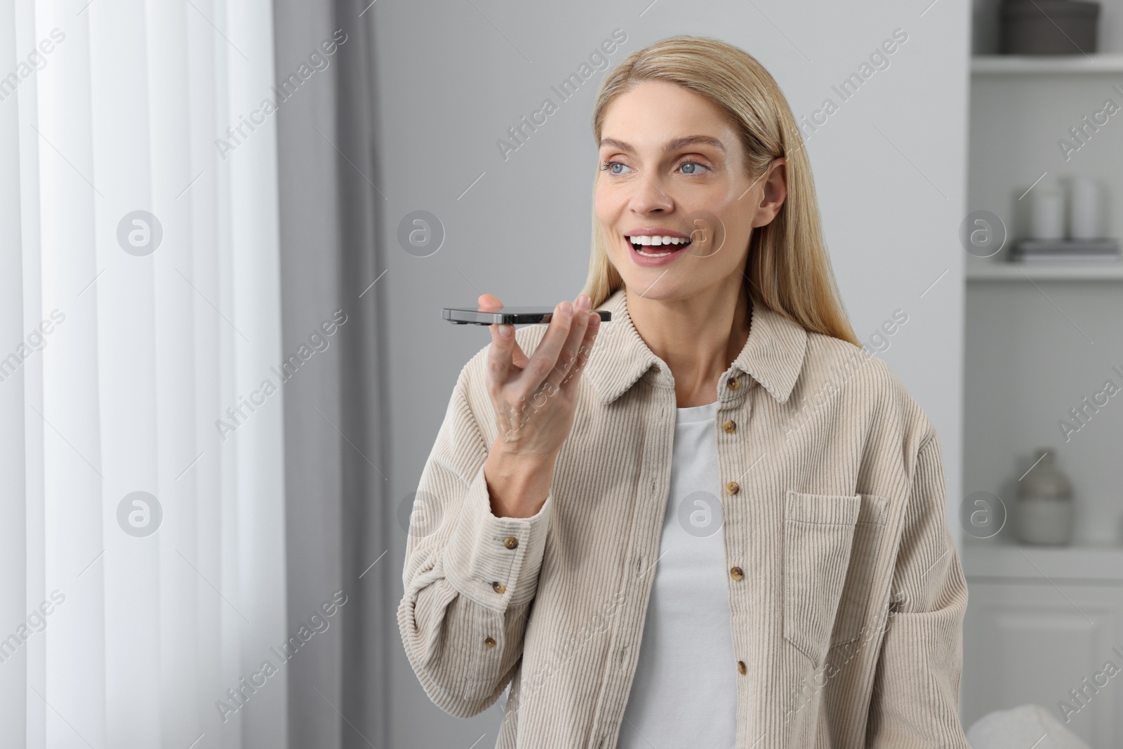 Photo of Woman recording voice message via smartphone at home, space for text