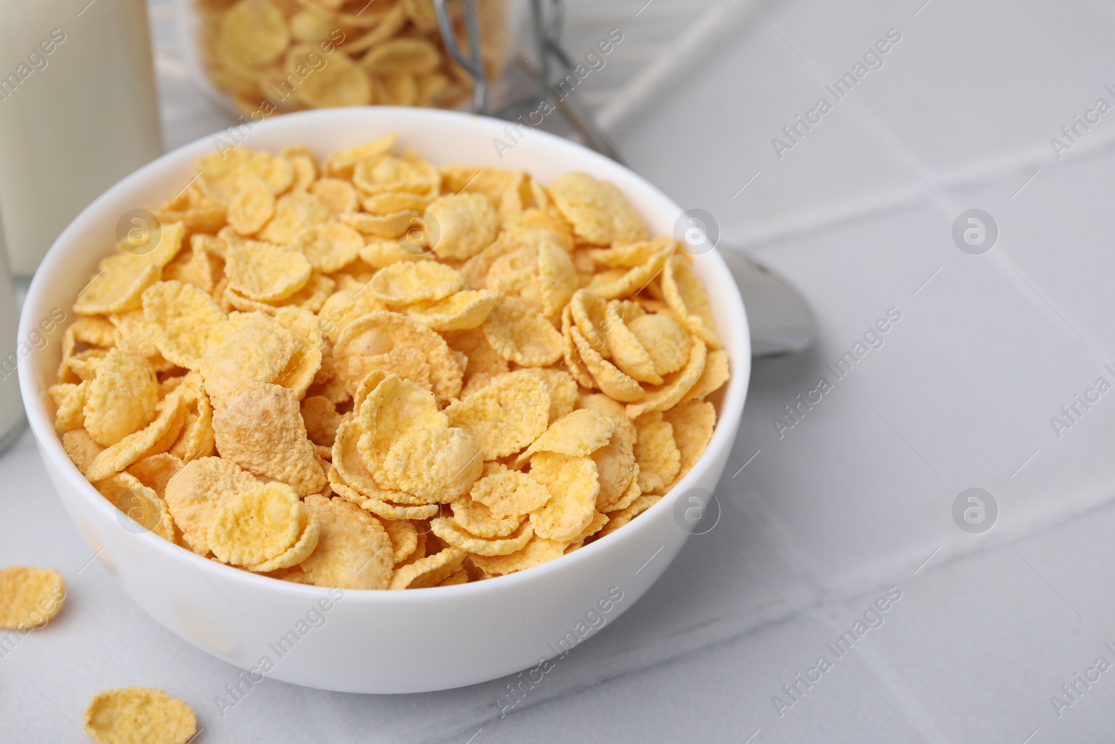 Photo of Breakfast cereal. Tasty crispy corn flakes in bowl on white tiled table, closeup. Space for text